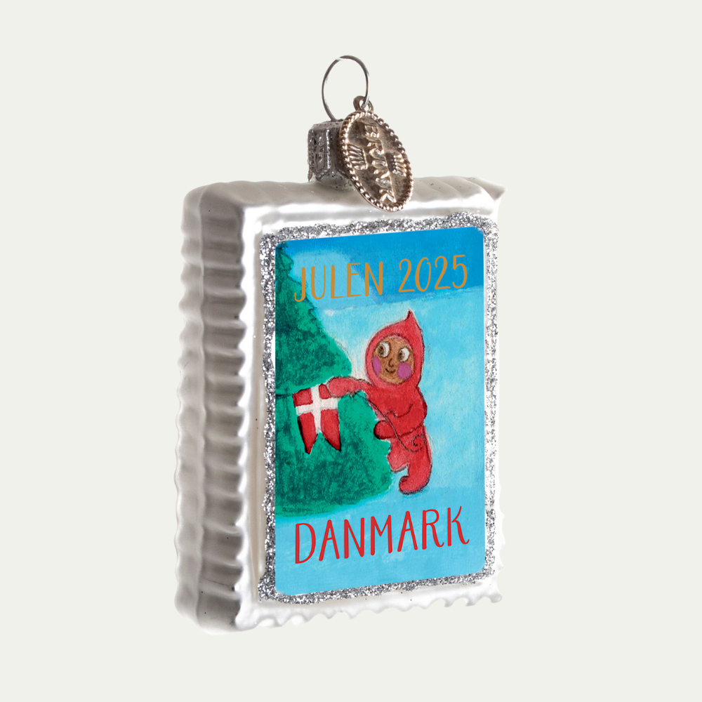 Julemærket 2025 Ornament. på ornamentet er der en nisse der sætter dannebrog på et juletræ